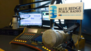 Desk at BPR showing a computer screen, microphone and the station's logo
