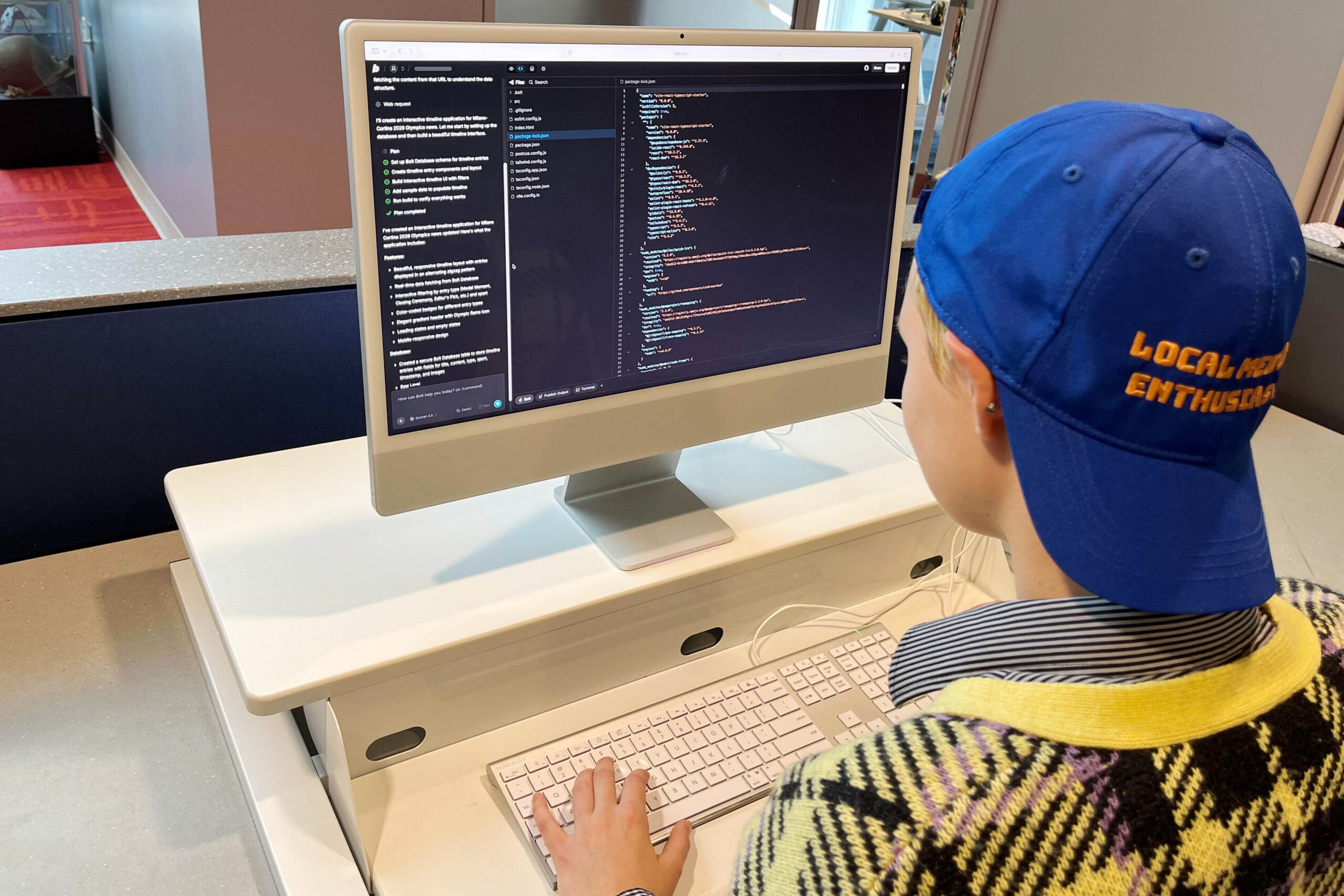 Woman works on computer showing code, wearing hat that says "local media enthusiast."