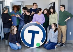 A group of adults stand around the Technical.ly logo